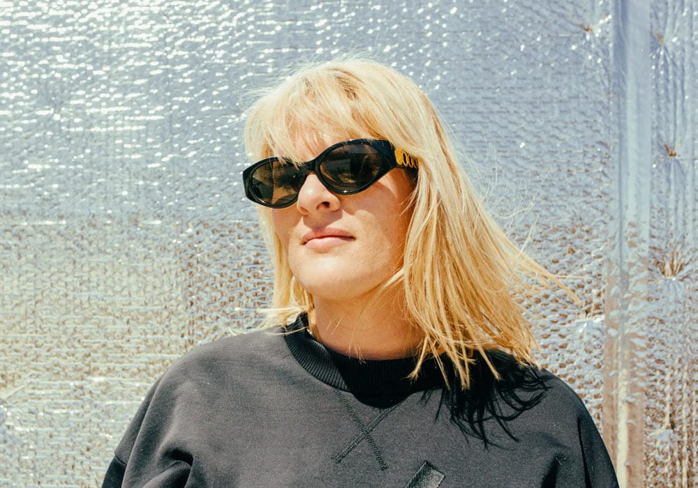 CC:DISCO! CC:DISCO! portrait. CC is wearing large black sunglasses and is standing in front of a silver reflective wall
