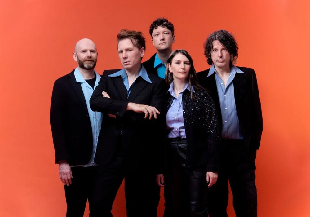 Franz Ferdinand band wearing black suits, posing in front of a bright orange backdrop