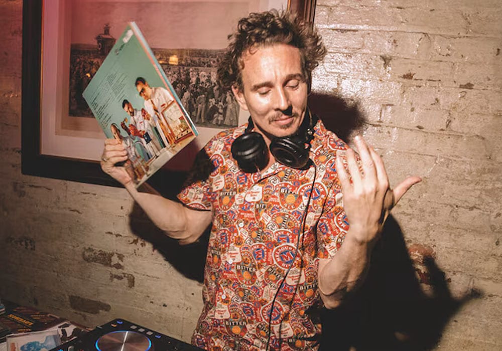 Joey Lightbulb behind the decks, holding a vinyl record