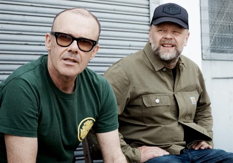 Leftfield band sitting outside in front of a roller door