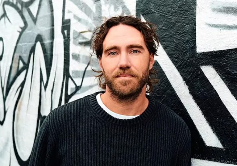Portrait or Matt Corby in front of a black and white graffiti wall