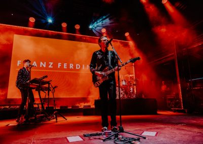 Franz Ferdinand performing on stage in the Royal Botanic Gardens Melbourne. Red lighting and band in the background.