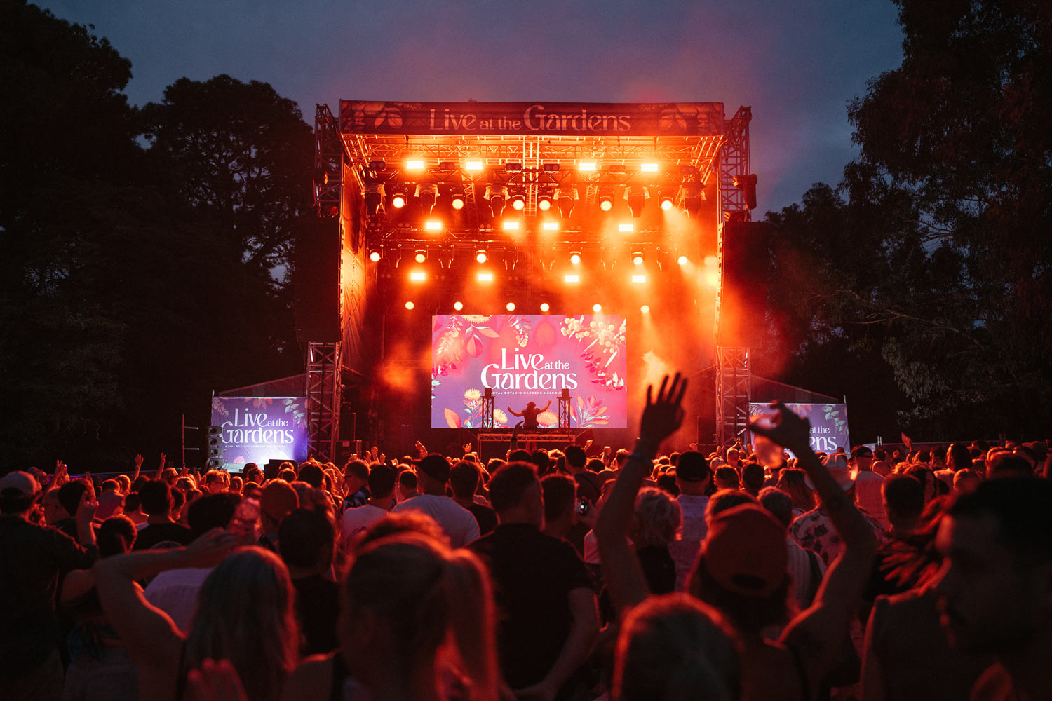 Live at the Gardens Stage 2025 with orange glowing lights and crowd dancing at night time.