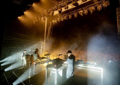 Electronic act Leftfield performing live on stage with keyboards and electronic equipment in front of a large crowd.