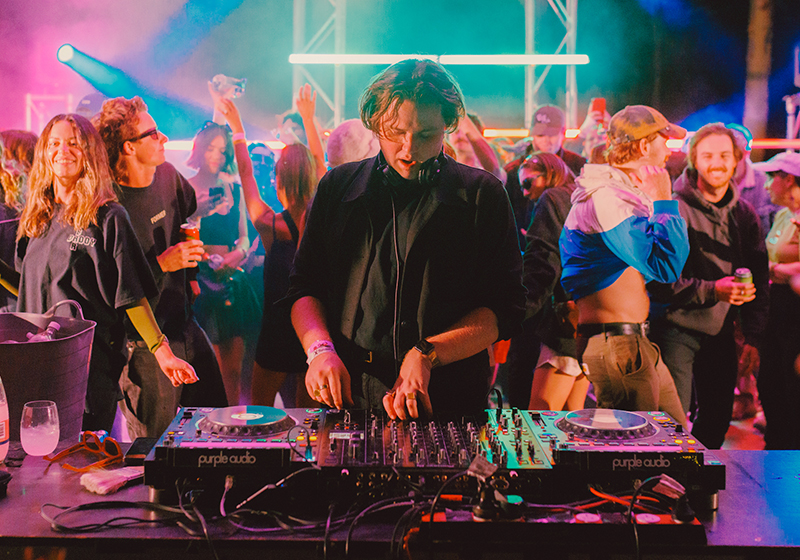 A photo of DJ Milo Eastwood performing in a warehouse with people dancing behind him